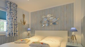 En pænt redt seng med to puder, et fiskespejl på væggen og en lampe på et natbord.