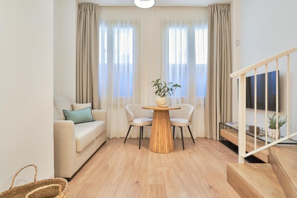 A living room with a sofa, two chairs, a round wooden table, and a TV on a stand.
