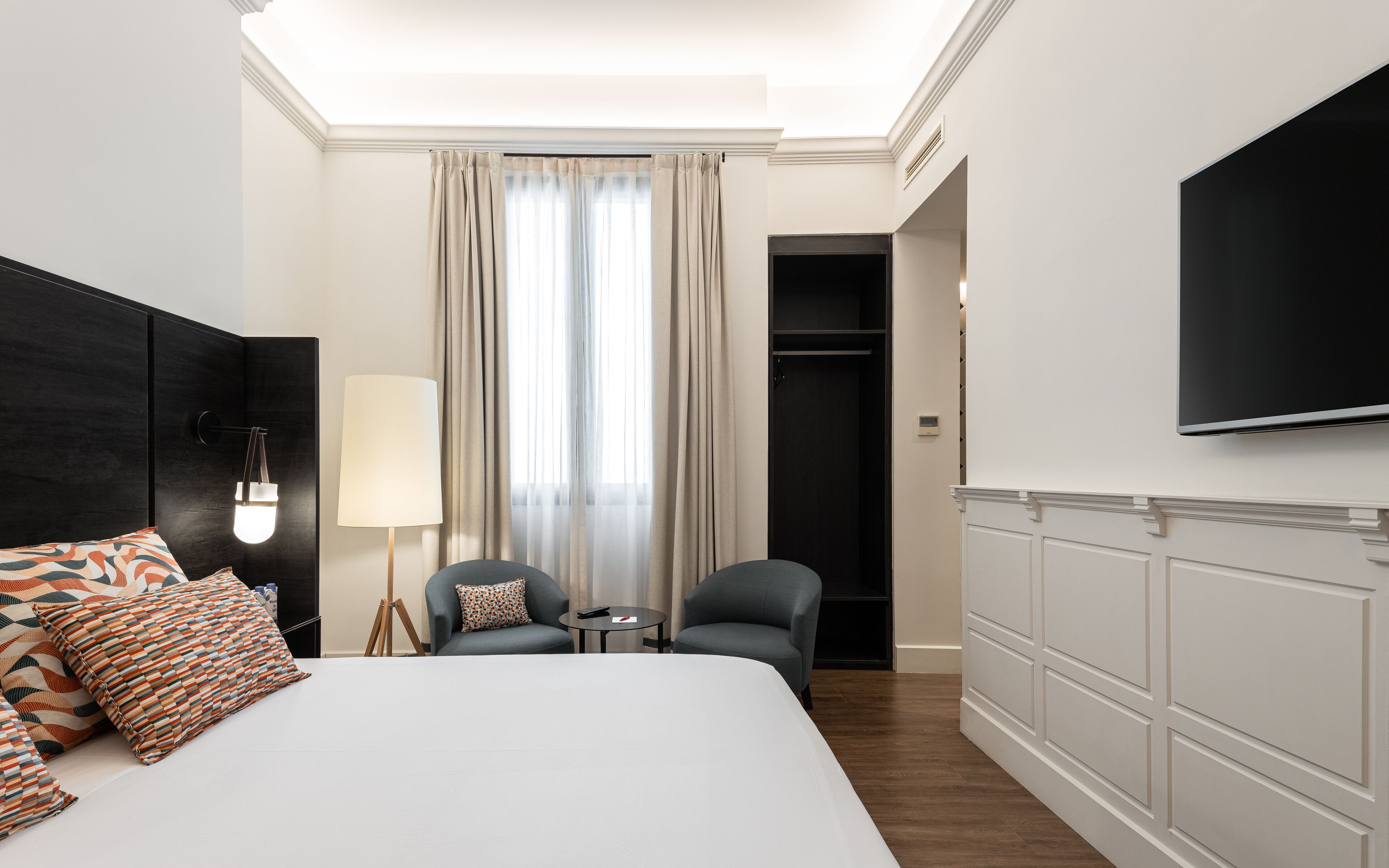 Une chambre d’hôtel avec un grand lit, un bureau, une chaise, une télévision et une armoire.