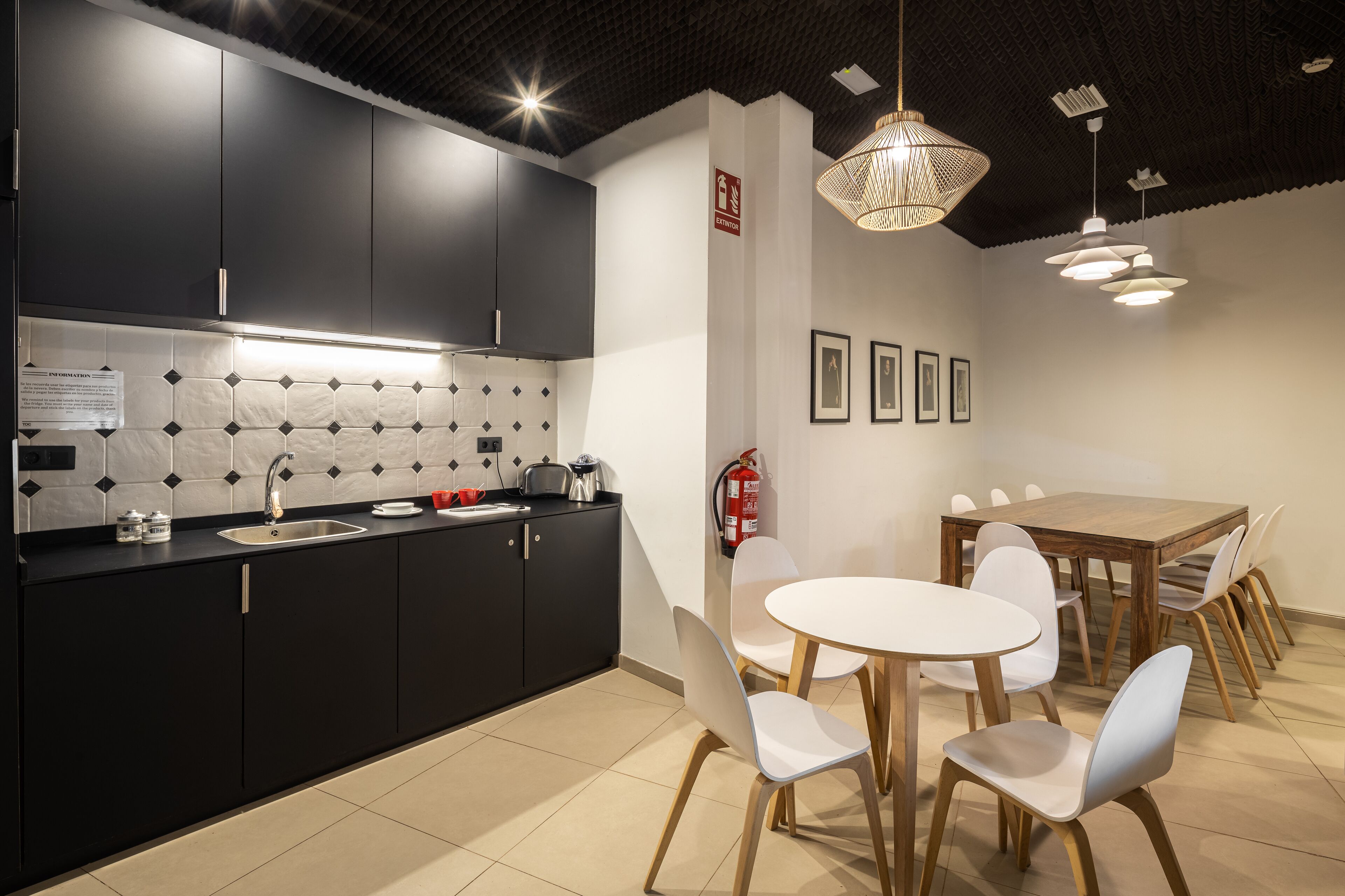 A modern kitchen with black cabinets, a white countertop, and a dining area with a wooden table and white chairs.