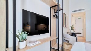 A modern hotel room with a flat-screen TV mounted on a wooden shelf, a small potted plant, and a neatly made bed. - TOC Hostel Málaga (Málaga)