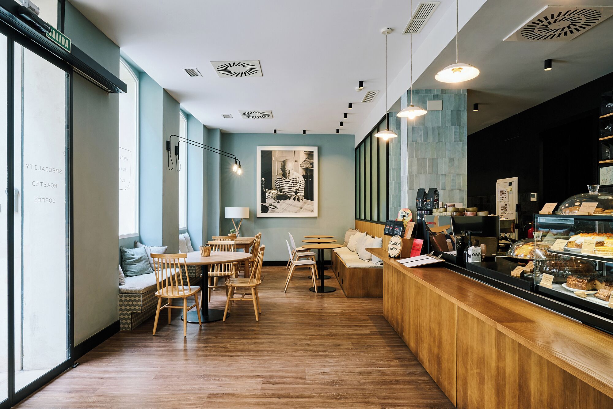 A cafe interior with wooden furniture, a counter with pastries, and a framed picture on the wall.