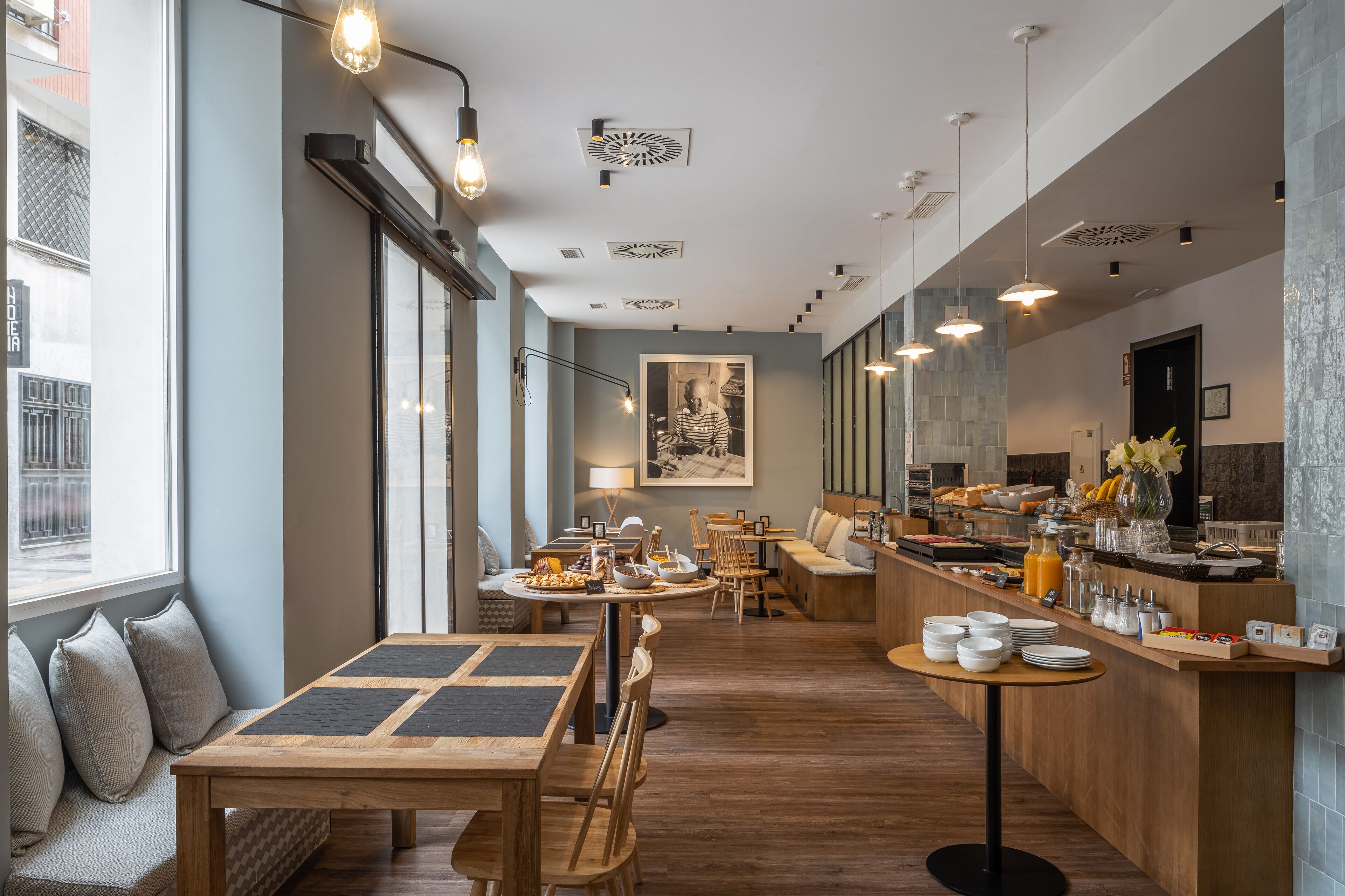 A modern cafe with wooden furniture, a buffet counter, and large windows.