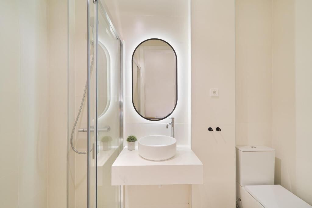 Ein modernes Badezimmer mit einem runden Waschbecken, einem Spiegel mit schwarzem Rahmen und einer Duschkabine aus Glas.