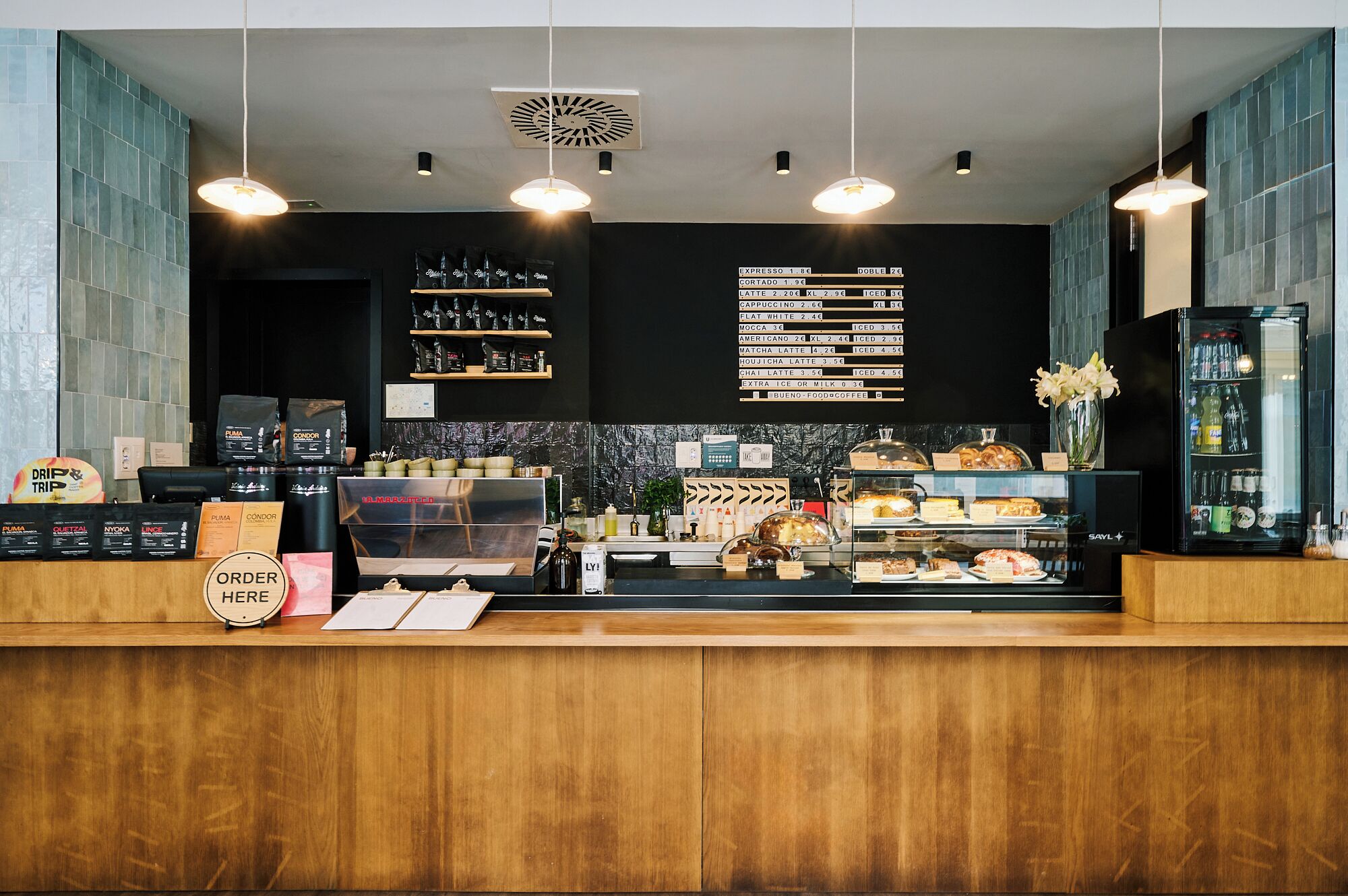 A coffee shop counter with a menu board, coffee machines, and a display of pastries.