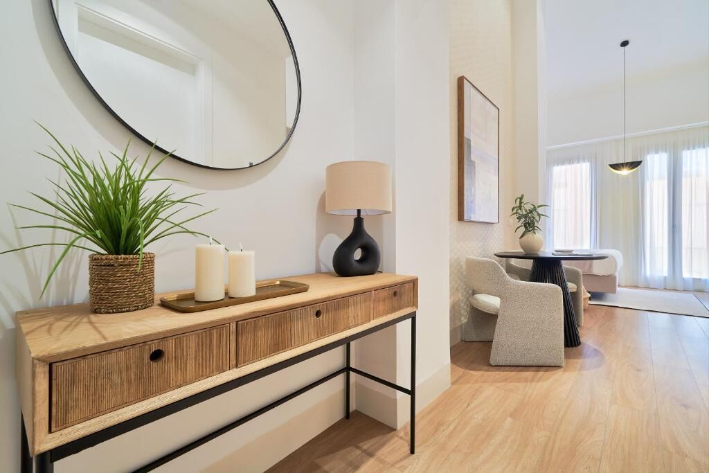 Una sala de estar moderna con una consola de madera, un espejo redondo, una lámpara y un sofá.
