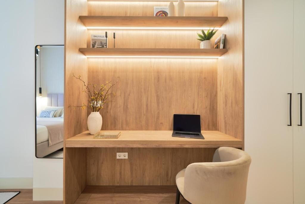 A modern workspace with a wooden desk, a laptop, a vase with branches, and a small plant.