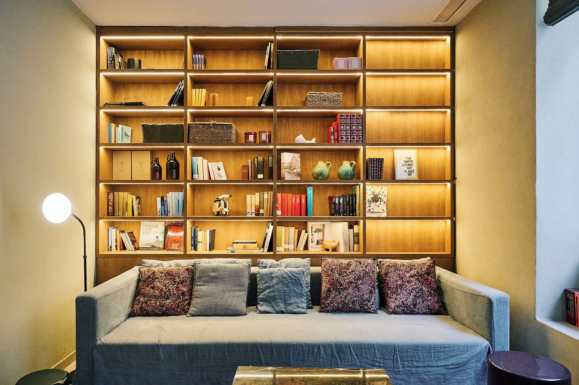A cozy living room with a large bookshelf filled with books and decorative items, a comfortable sofa with cushions, and a floor lamp.