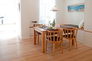 Et spiseområde med et træbord og stole, en vase med blomster og et maleri på væggen.