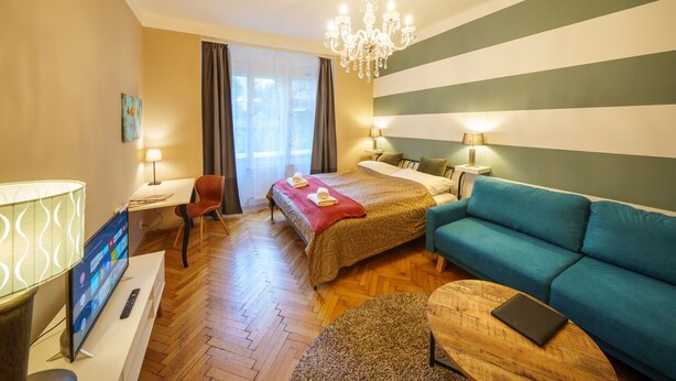 Ein Hotelzimmer mit Bett, einer Couch, einem Fernseher, einem Schreibtisch und einer Chandelier.