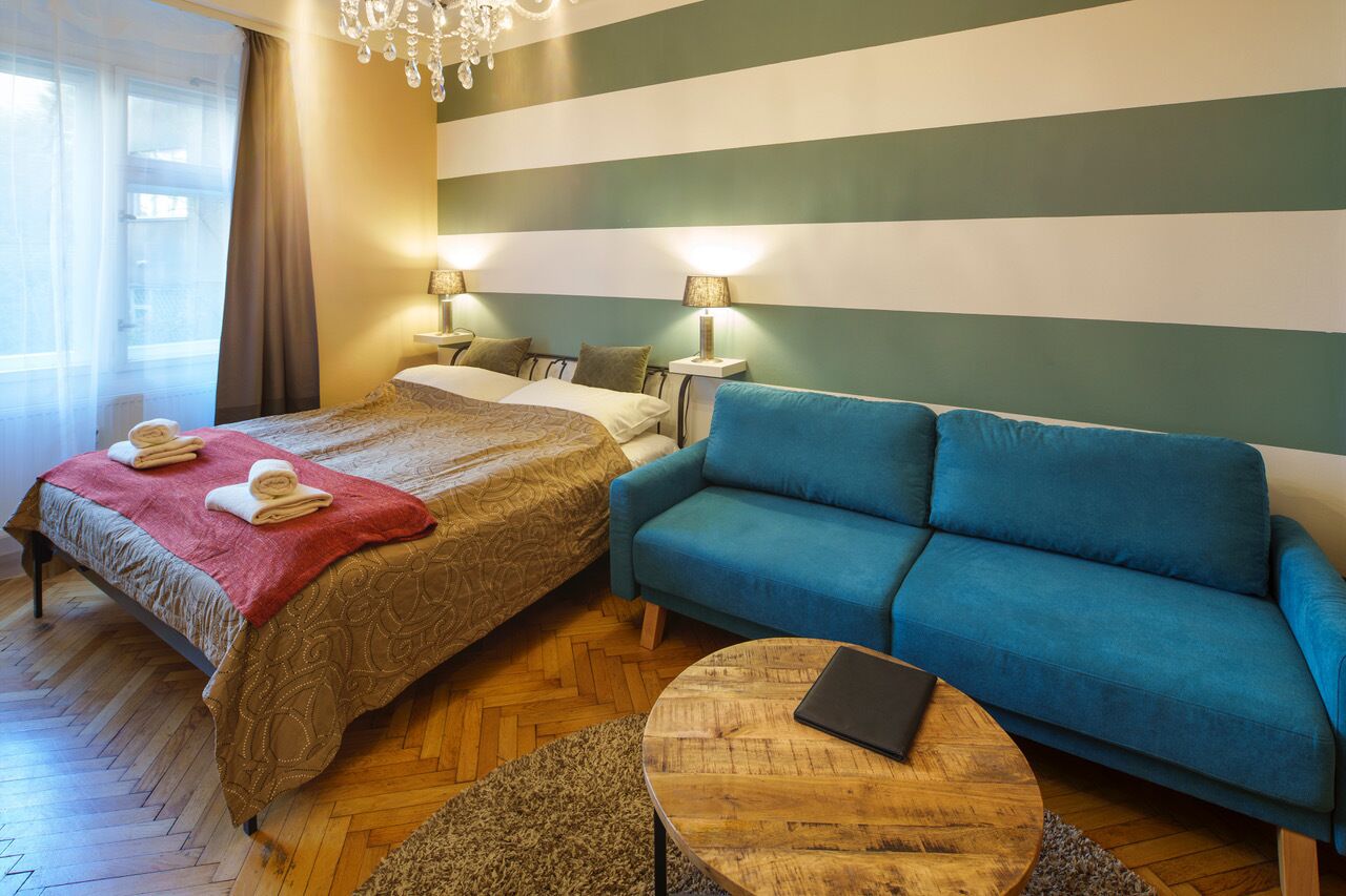 Habitación de hotel con una cama, un sofá azul, una mesa redonda de madera y una araña.
