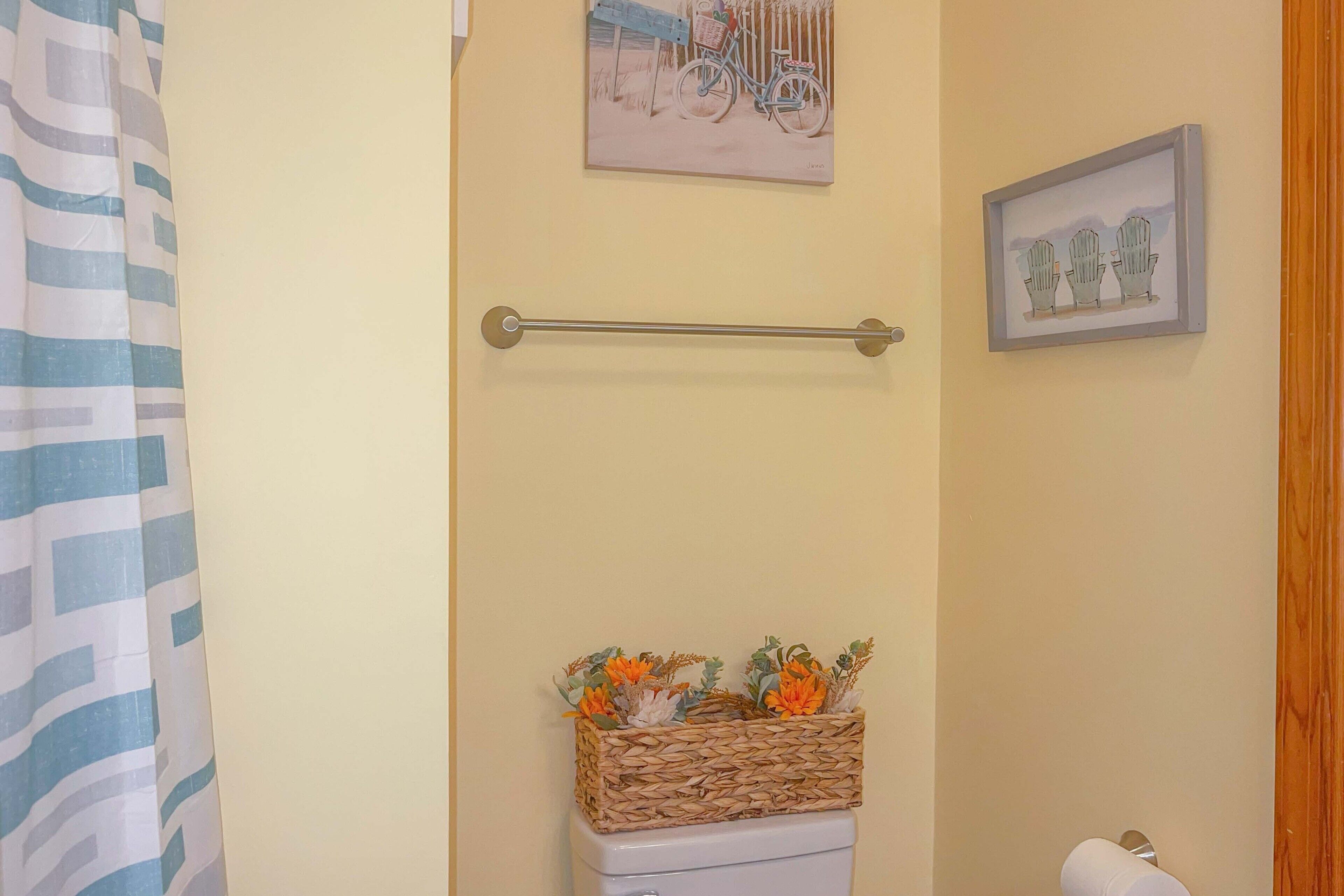 A bathroom with a towel rack, a wicker basket with flowers, and two framed pictures on the wall.