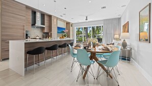 A modern kitchen with a central island, bar stools, and a dining area with a round table and chairs. - Heated Pool, Modern Spacious Waterway Home Offering Comfort, Style & Total Relaxation! (Wilton Manors)