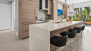 A modern kitchen with wooden cabinetry, stainless steel appliances, and a large island with bar stools. - Heated Pool, Modern Spacious Waterway Home Offering Comfort, Style & Total Relaxation! (Wilton Manors)