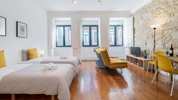 Habitación de hotel con dos camas, zona de comedor, televisor y pared de piedra.