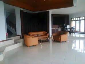 A spacious living area with a sofa and armchairs, a staircase, and a kitchen area.