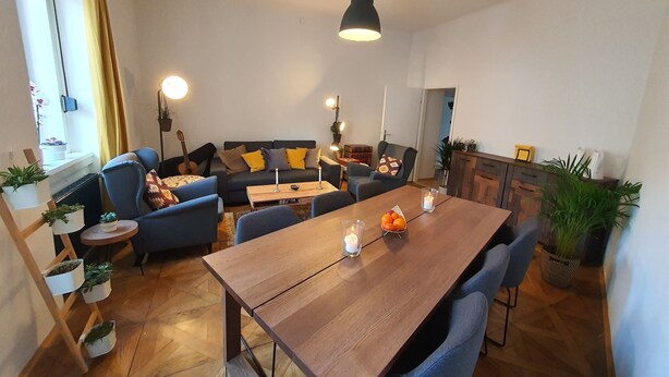 A cozy living room with a wooden dining table, blue sofas, and a guitar. - Central Graz Apartments by Paymán Club (Graz)