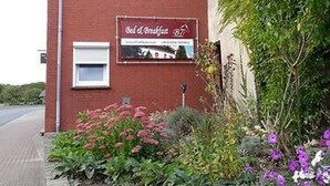 Un bâtiment en briques rouges, avec une enseigne indiquant « chambre d’hôtes », et un jardin agrémenté de fleurs et d’arbustes.