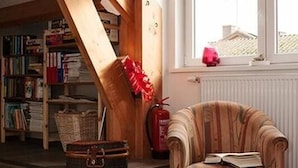 Une pièce chaleureuse avec un escalier en bois, un fauteuil à carreaux, une bibliothèque et une fenêtre donnant sur un beau paysage.