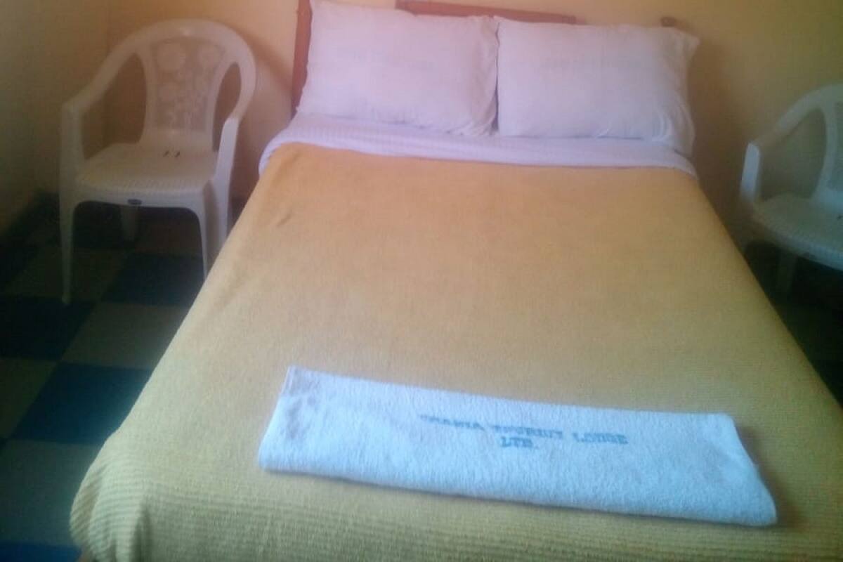 A single bed with a white headboard and pillows, a white chair to the left, and a white chair to the right.