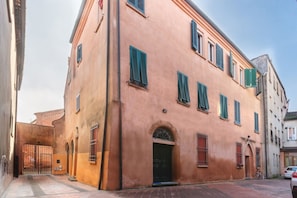 Un edificio con un amplio acceso de arco, varias ventanas con contraventanas y una entrada portonada.