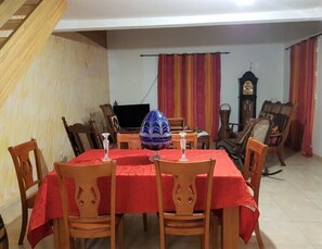 Un coin repas avec une nappe rouge, des chaises en bois et un grand saladier décoratif.