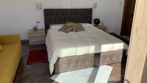 Quarto com uma cama grande, uma mesa de cabeceira, um abajur e uma cadeira.