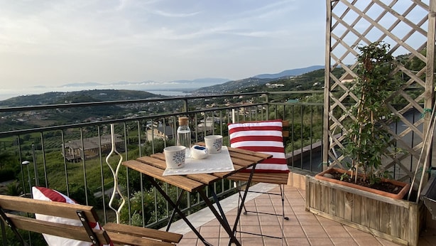 Una terraza con una mesa de madera, dos sillas, una maceta y vistas a un paisaje lejano.