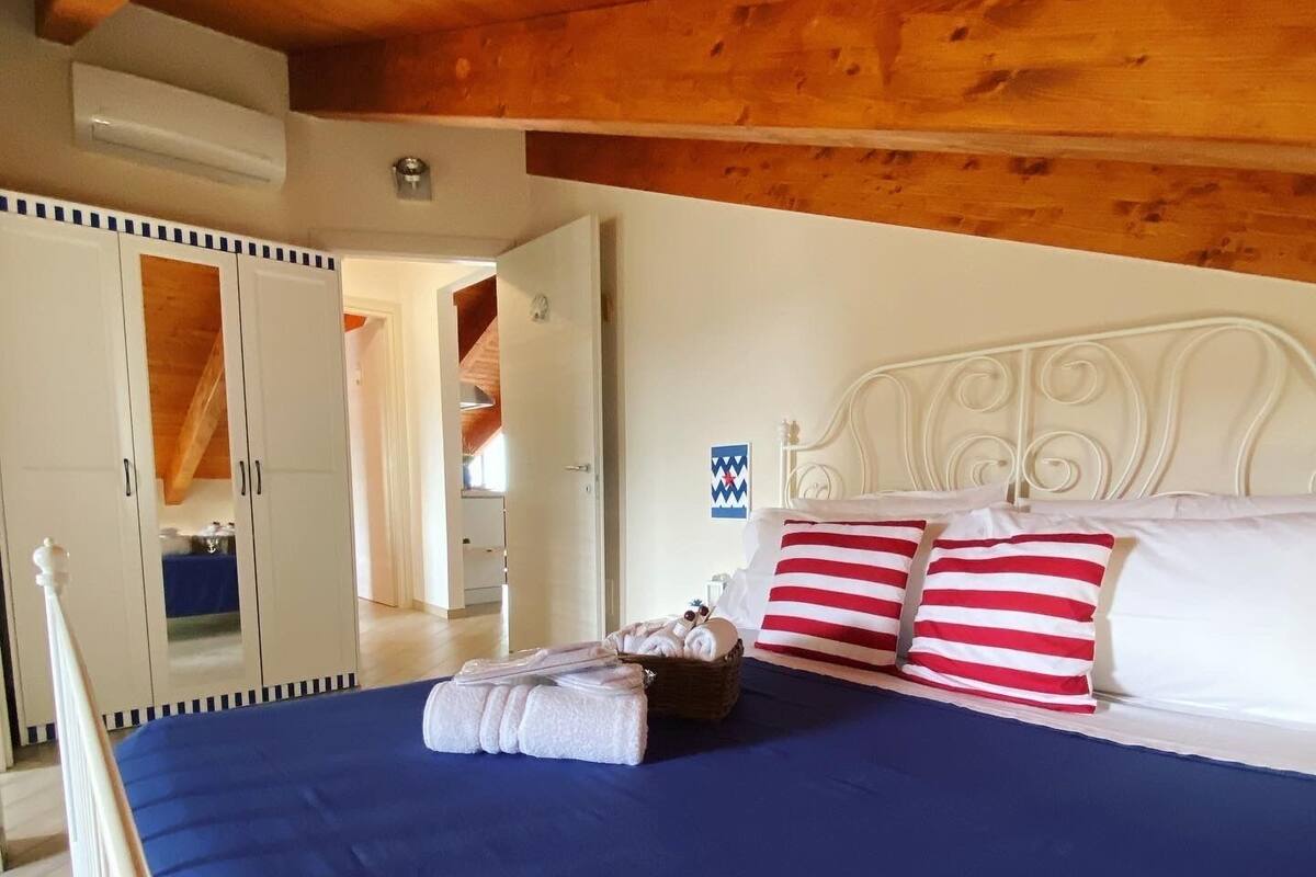 A bedroom with a large bed, wooden ceiling beams, a wardrobe, and a small wall decoration.