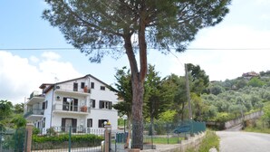 Un edificio residencial de dos pisos con fachada blanca, varios balcones y un árbol grande en la parte delantera.