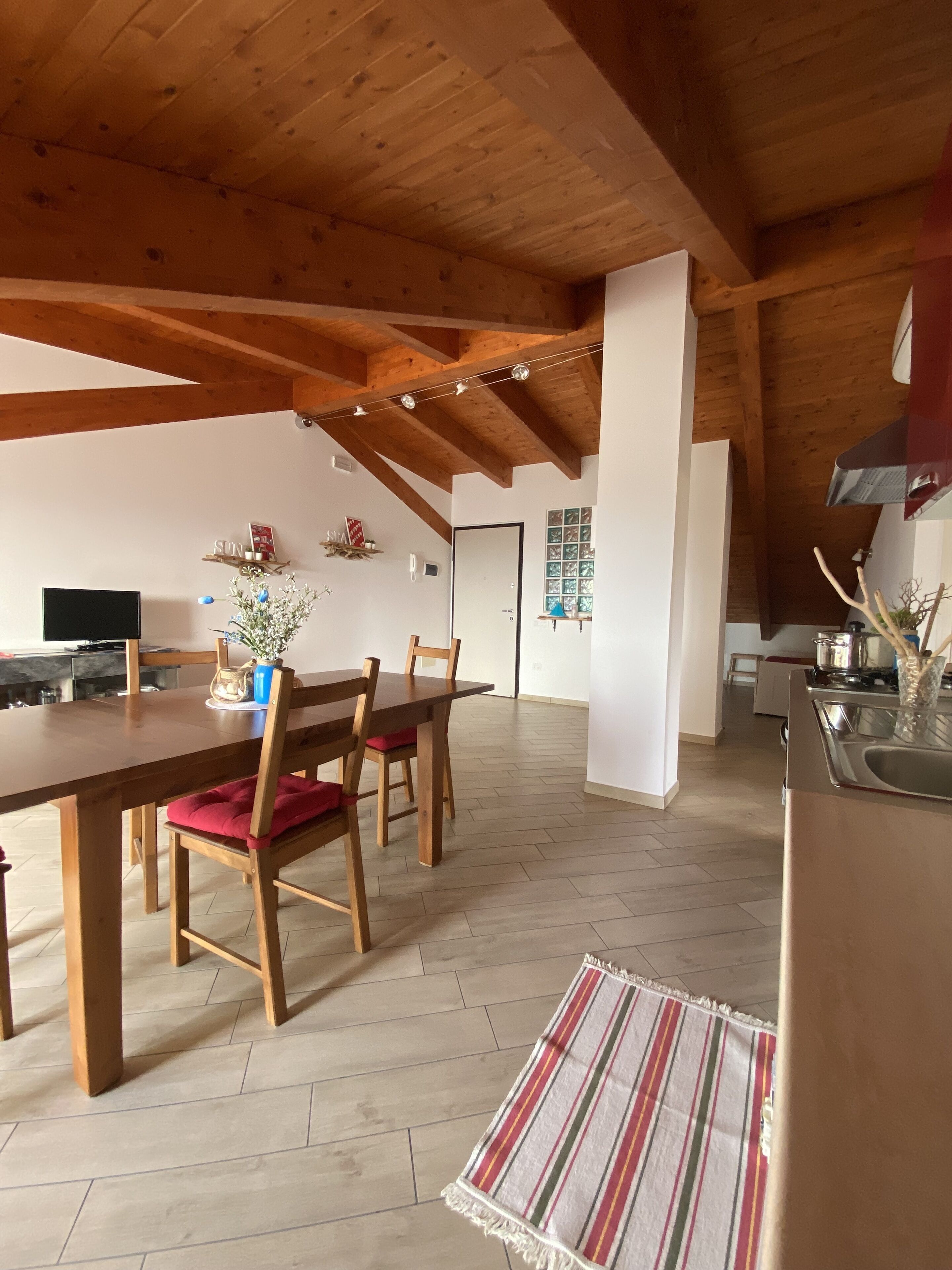 Un vaste espace dédié à la salle à manger, avec une table et des chaises en bois, une cuisine en arrière-plan et un parquet à motifs en chevrons.