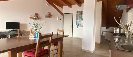 Un vaste espace dédié à la salle à manger, avec une table et des chaises en bois, une cuisine en arrière-plan et un parquet à motifs en chevrons.
