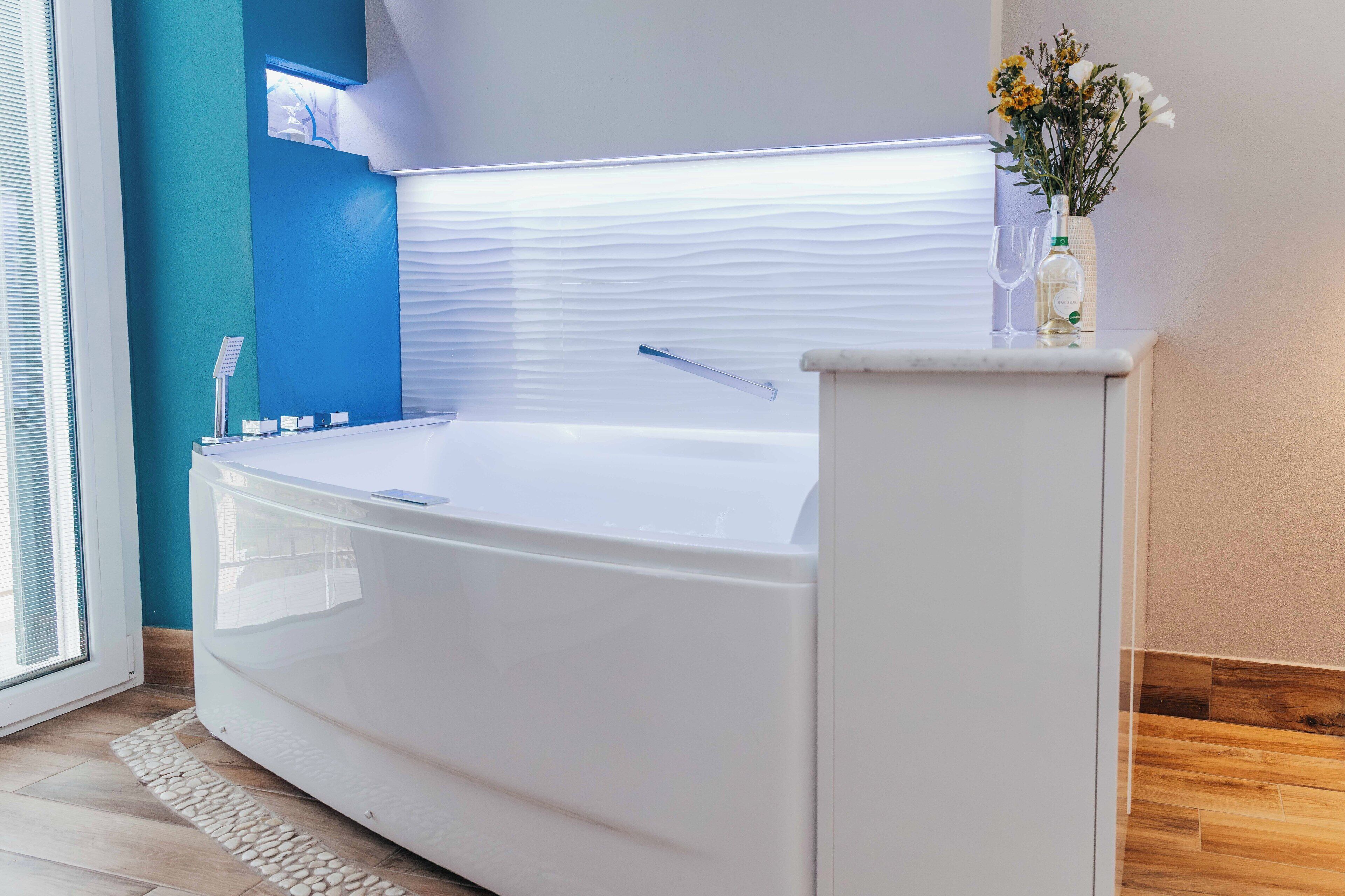 A modern bathroom with a large bathtub, a glass shower enclosure, and a small table with a bottle and glass.