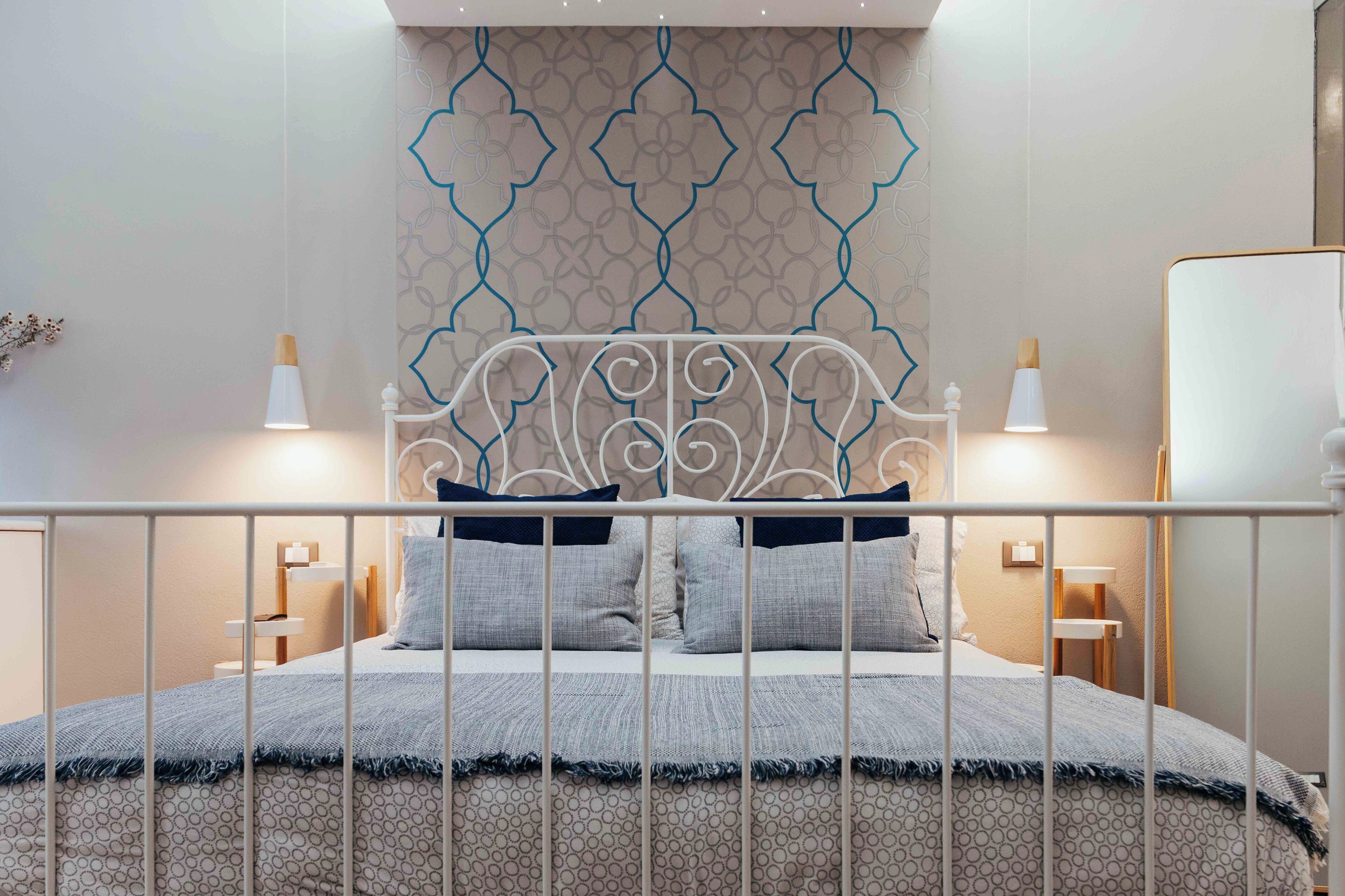 A neatly arranged bedroom with a patterned headboard, a bed with grey bedding, and two bedside lamps.