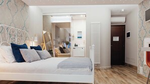 Un dormitorio moderno con una cama blanca, suelo de madera y una puerta de cristal que da al baño.