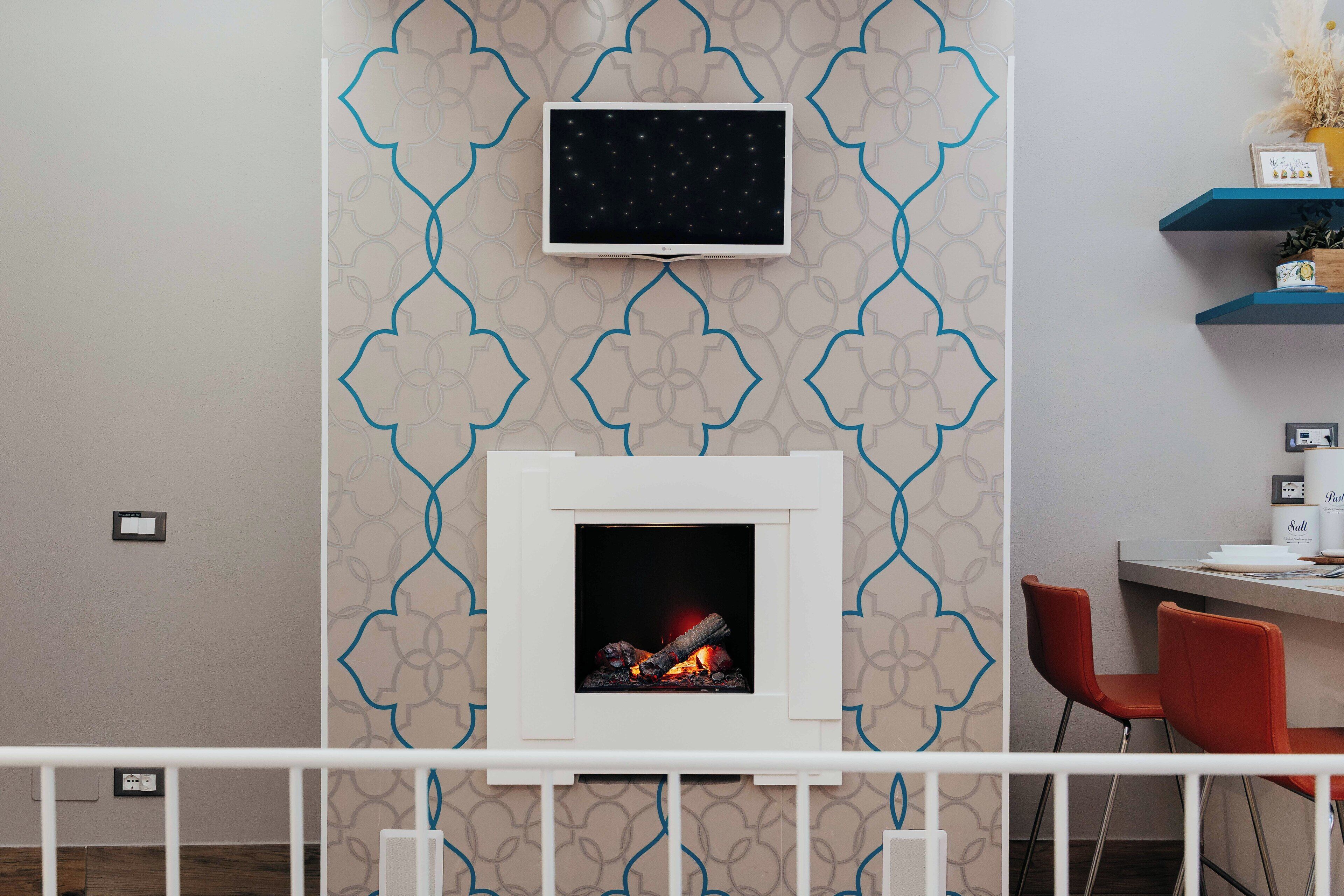 Una habitación moderna con chimenea, televisor montado y una pequeña mesa con sillas.