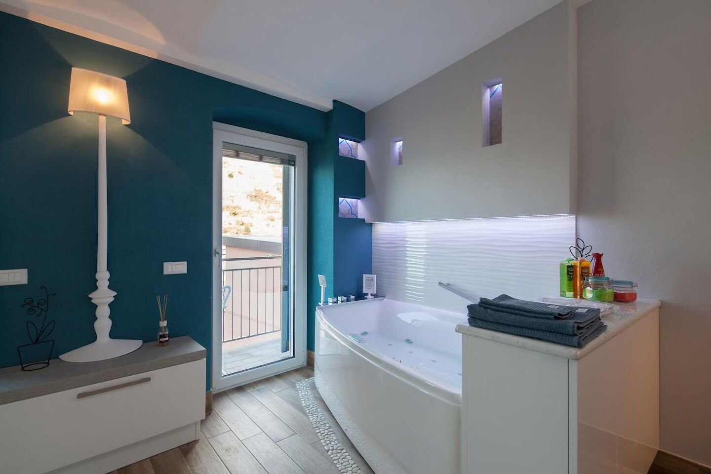 Un bagno moderno con una vasca, un mobile lavabo bianco, una lampada da terra e una porta finestra.
