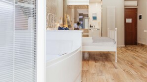 Un dormitorio moderno con una cama blanca, una mesita de noche, un espejo y suelo de madera.