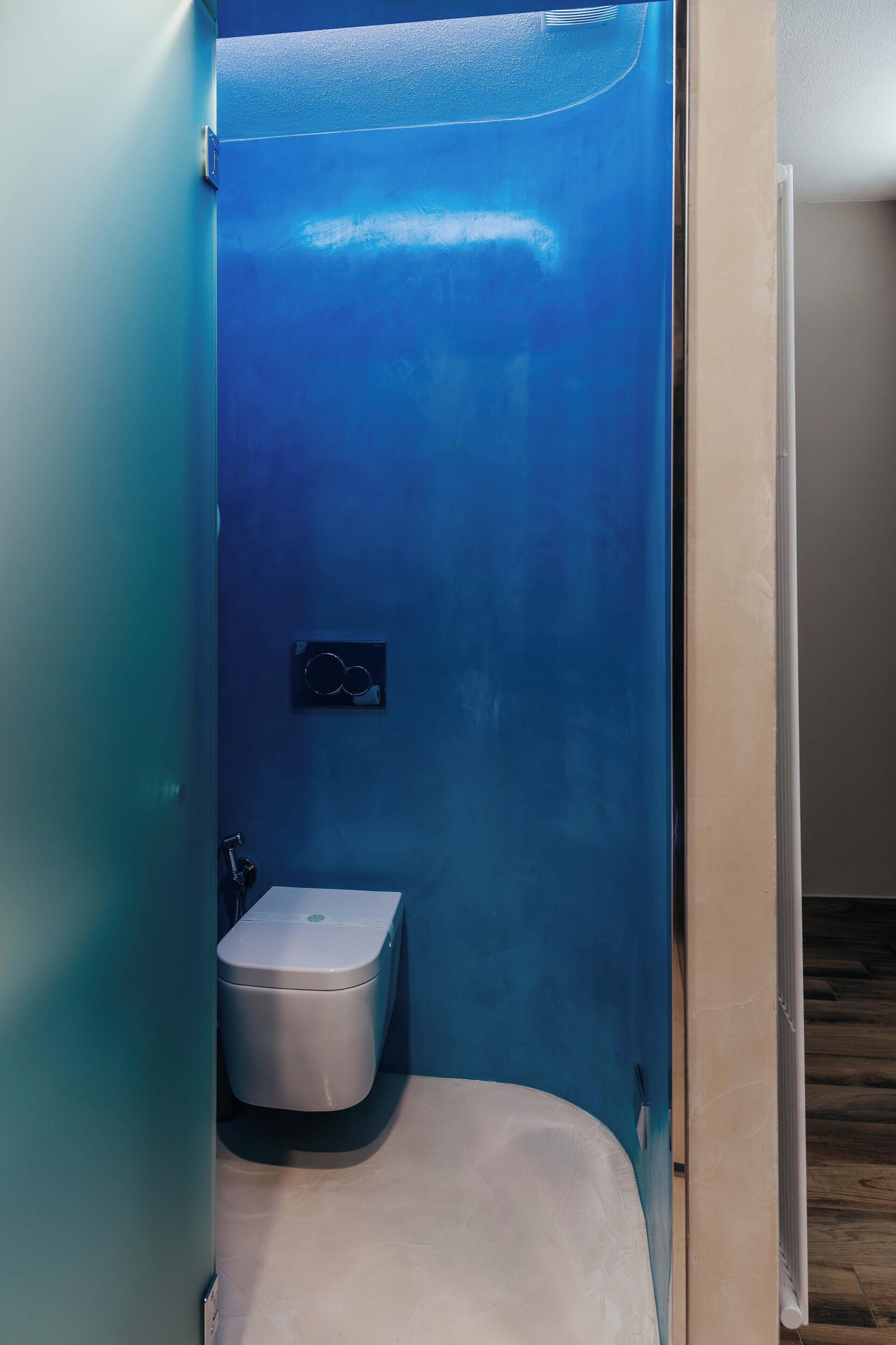 A small, enclosed bathroom with a toilet and a wall-mounted flush handle.
