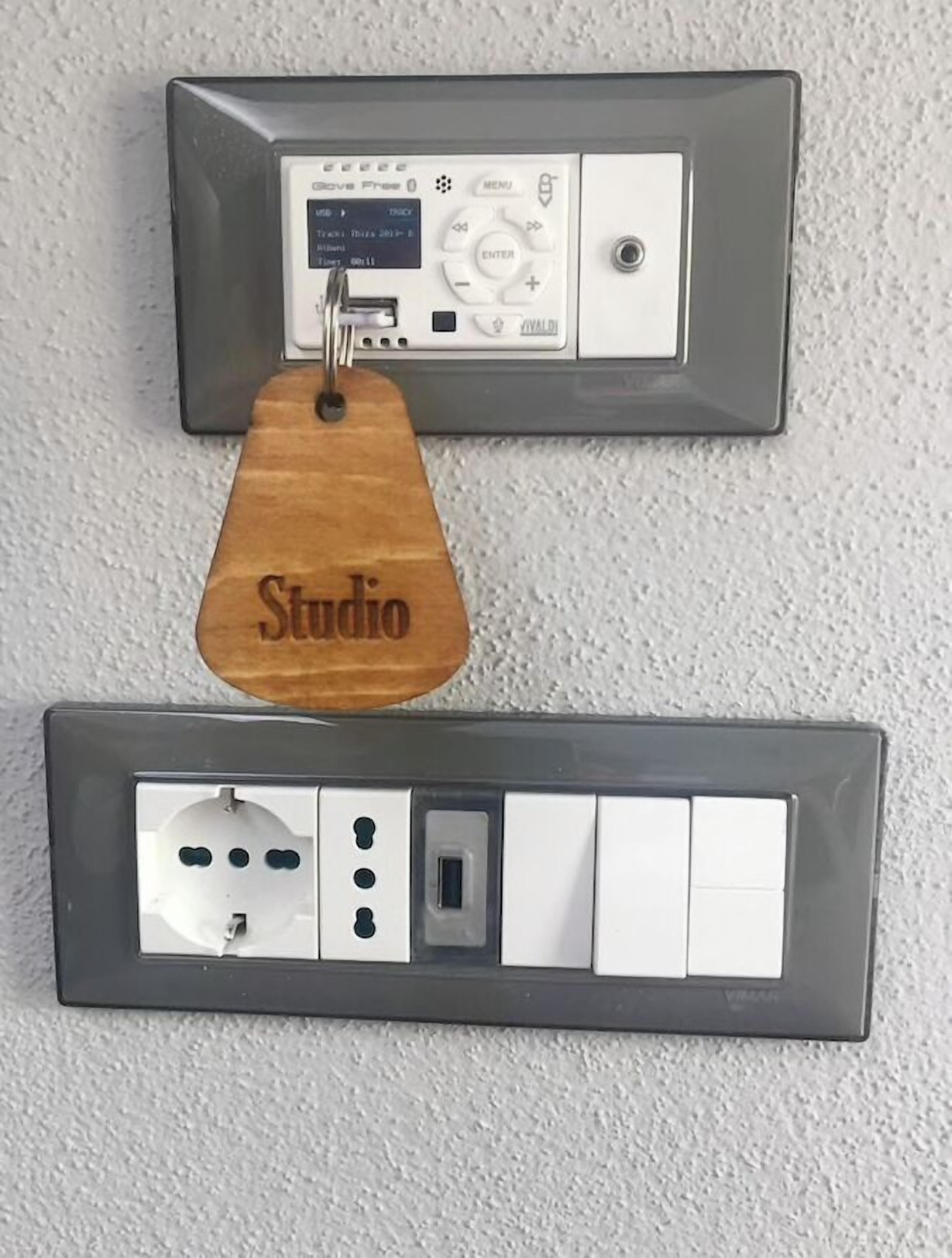 A wall-mounted electrical panel with a wooden tag labeled "Studio" and a switchboard below it.