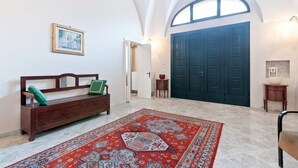 A spacious room with a high arched ceiling, a large dark door, a wooden bench with cushions, a patterned rug, and a framed picture on the wall. - GuestHost - Terrace Apartment 20 minutes from Lecce (Squinzano)