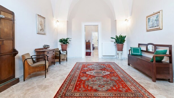 A hallway with a red patterned rug, wooden furniture, potted plants, and framed artwork on the walls. - GuestHost - Terrace Apartment 20 minutes from Lecce (Squinzano)