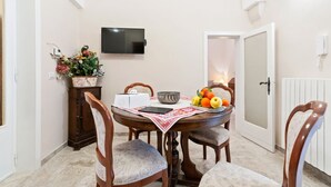 A dining area with a round table, chairs, a TV mounted on the wall, a door, and a radiator. - GuestHost - Terrace Apartment 20 minutes from Lecce (Squinzano)