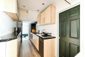 A narrow kitchen with wooden cabinets, a black countertop, and a green door.