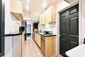 A compact kitchen with wooden cabinets, a black countertop, and a dark door.