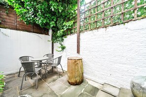A patio area with a table and chairs, a wooden stump, and a white brick wall. - Spacious and bright just-renovated flat with patio (London)