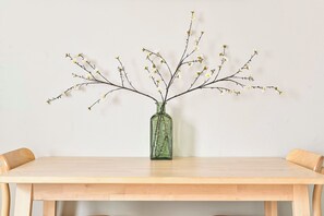 A wooden table with a green glass vase containing branches with small white flowers. - Spacious and bright just-renovated flat with patio (London)