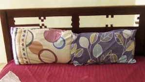 A bed with a red bedspread, two pillows with floral patterns, and a folded white towel. - Crestone Peak Inn Guest House (Nairobi)