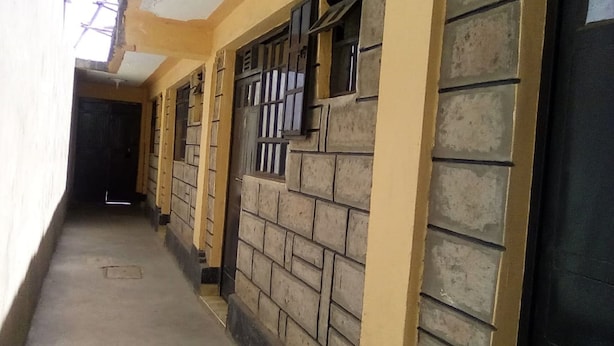 A corridor with a tiled floor, yellow walls, and a black door at the end. - Crestone Peak Inn Guest House (Nairobi)
