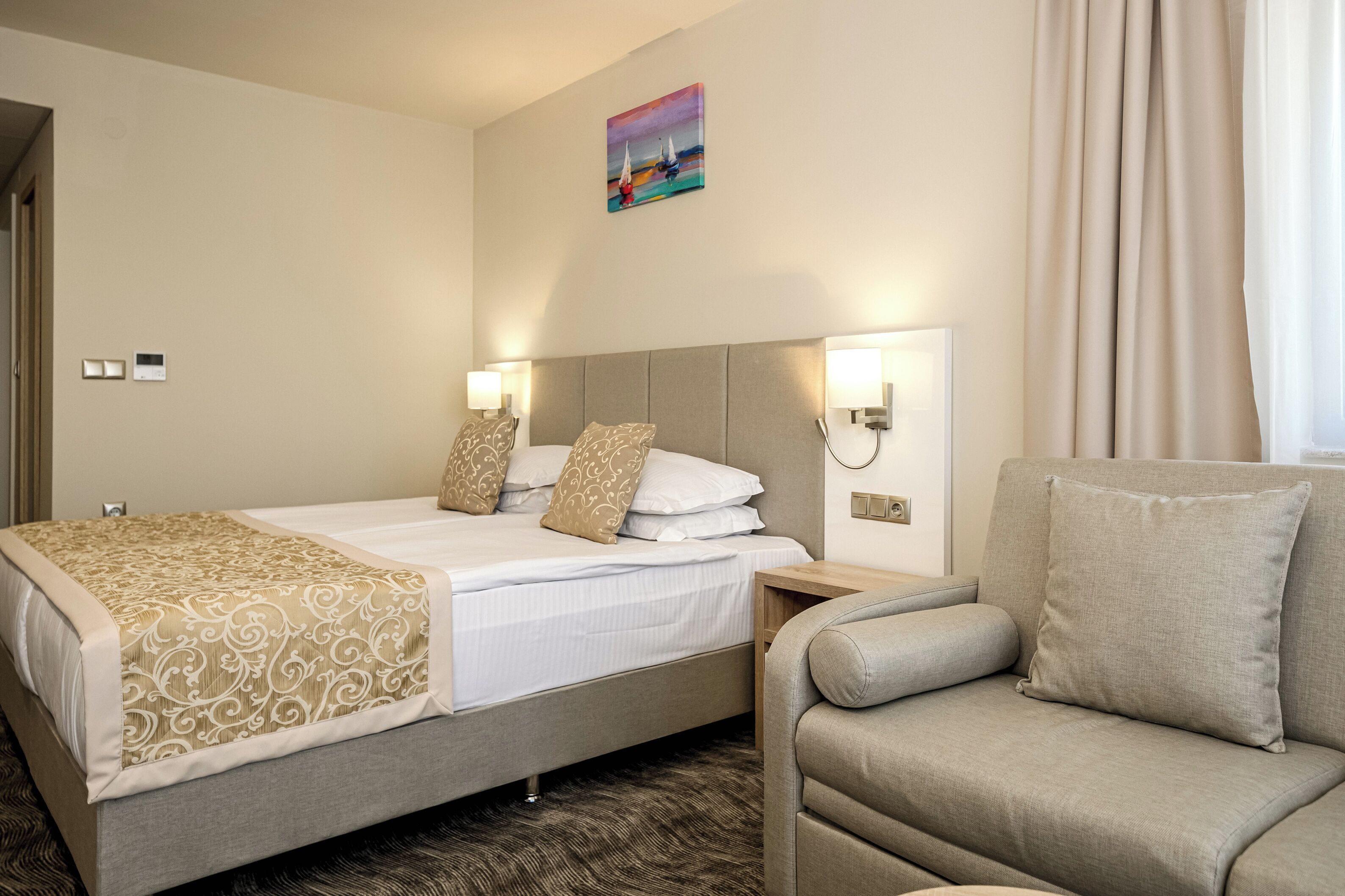 Une chambre d’hôtel avec un lit, deux lampes de chevet, une table de chevet, un canapé et un tableau au mur.